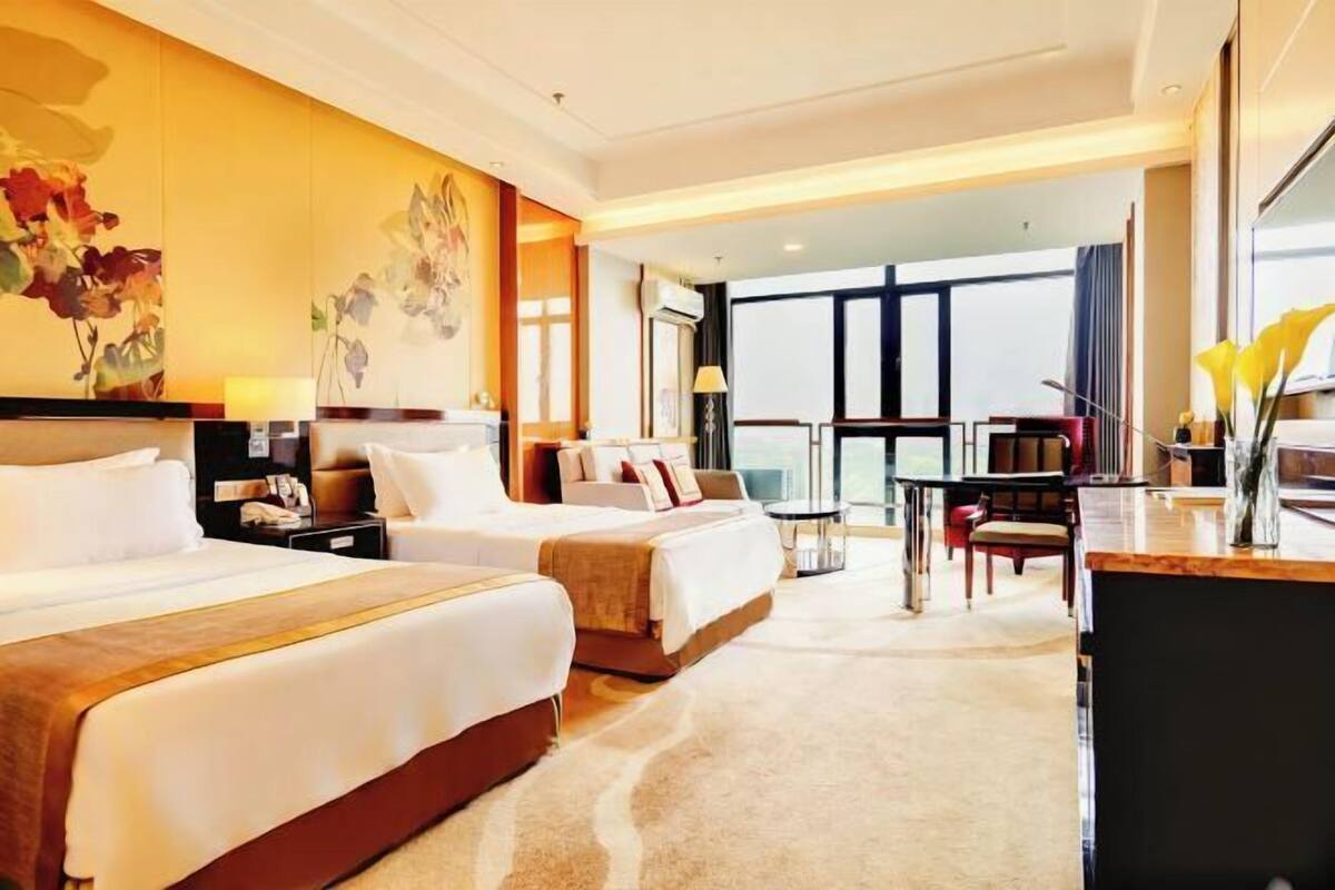 A hotel room with two beds, a desk, a chair, and a large window.