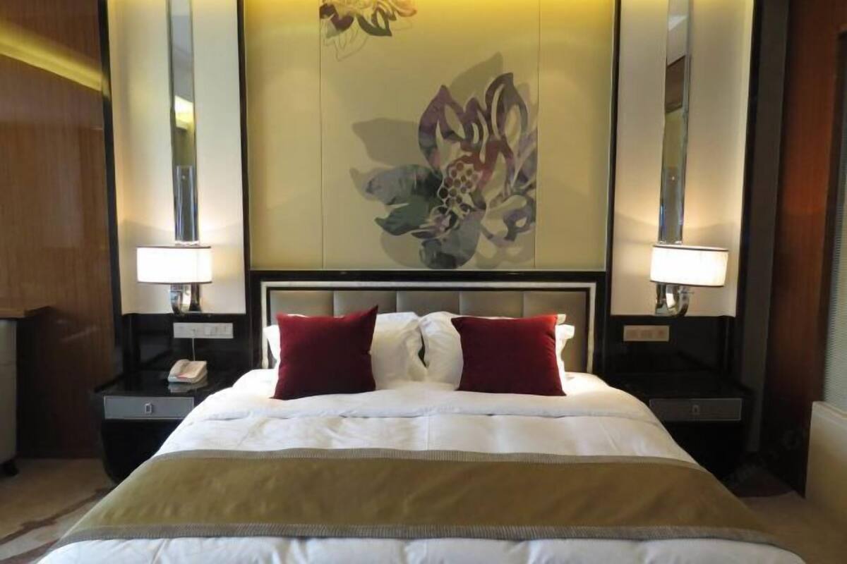 A hotel room with a large bed, two bedside lamps, a nightstand with a phone, and a decorative wall panel.