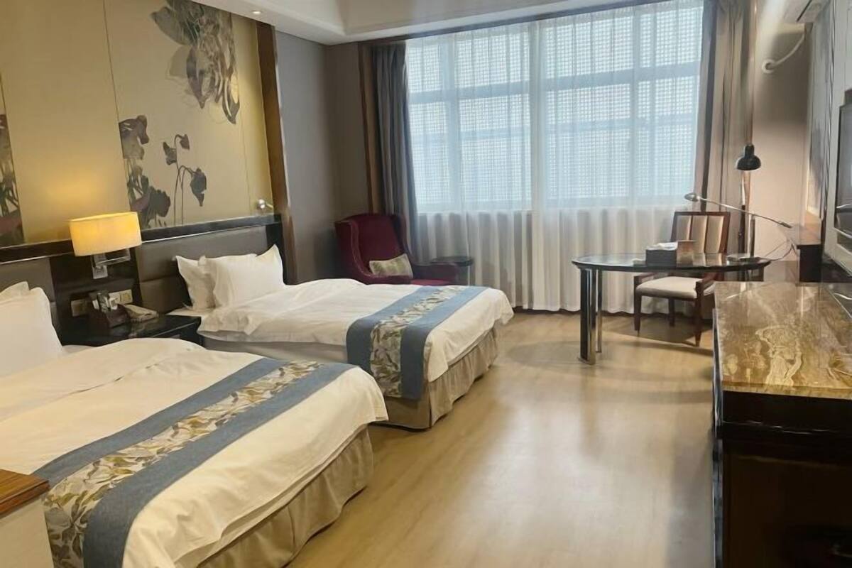 A hotel room with two beds, a desk, a chair, and a large window with curtains.