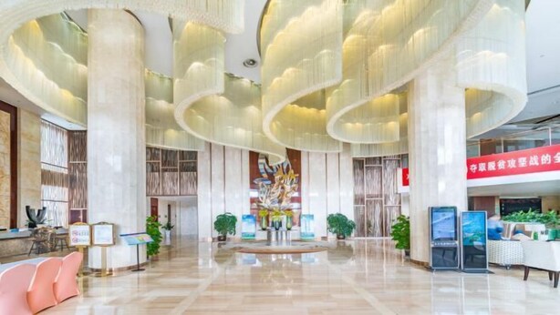 A spacious lobby with a modern design, featuring a central art installation, seating areas, and a reception desk.