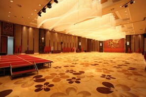 A large hall with a stage and rows of chairs, carpeted floor, and a high ceiling with lighting fixtures. - Doreen Hotel (Lianshui)
