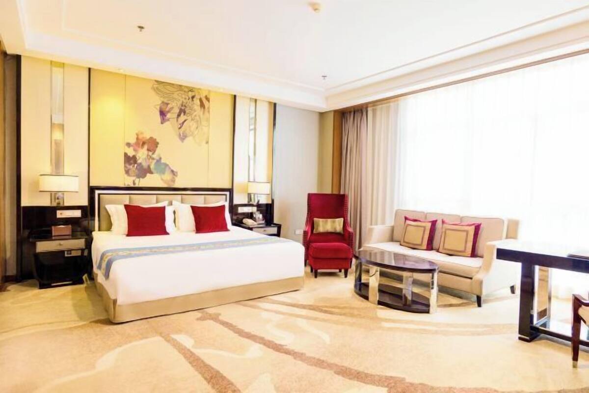 A hotel room with a large bed, a sofa, a chair, a small table, and a painting on the wall.