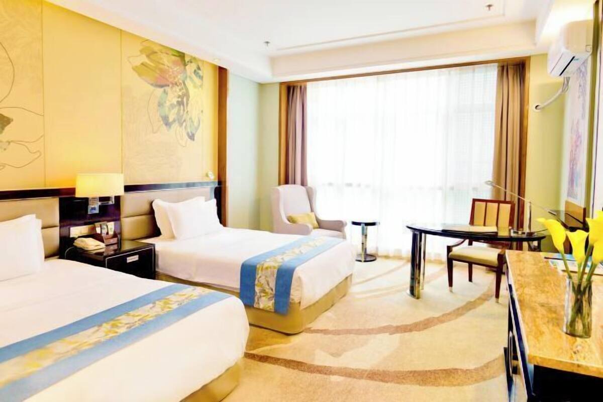 A hotel room with two beds, a desk, a chair, a small table, and a window with curtains.