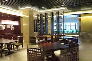 A restaurant interior with tables and chairs, a decorative wall with shelves, and a view through a window. - Doreen Hotel (Lianshui)