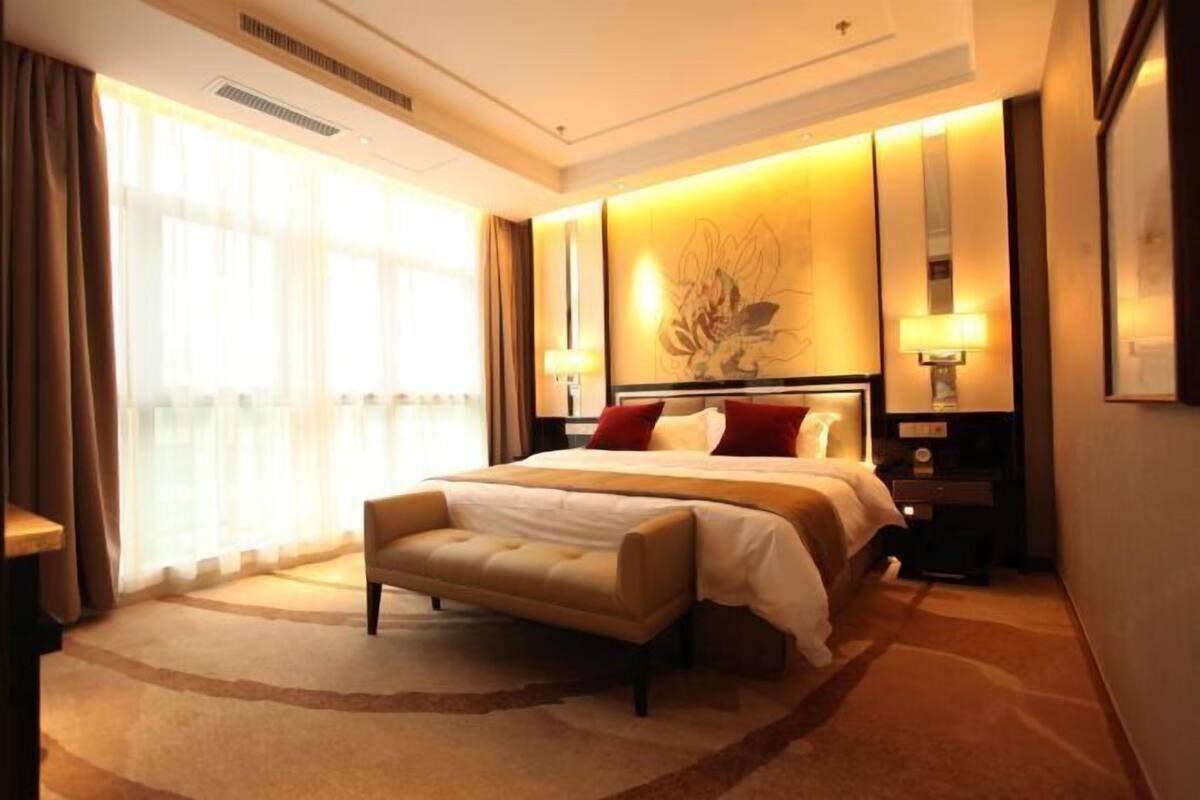 A hotel room with a large bed, a bench, a nightstand, and a wall-mounted lamp.