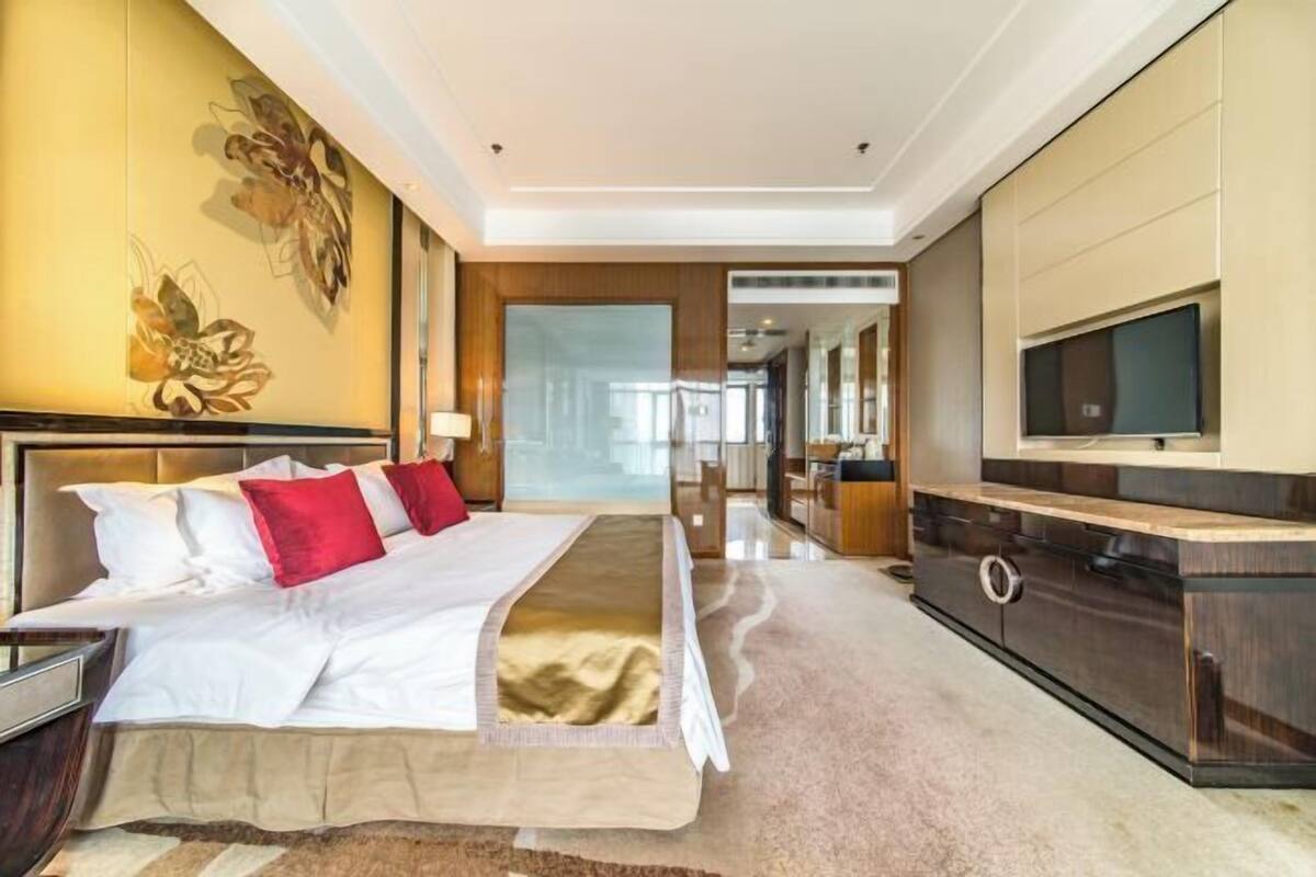 A modern hotel room with a large bed, a TV, and a view of the hallway.