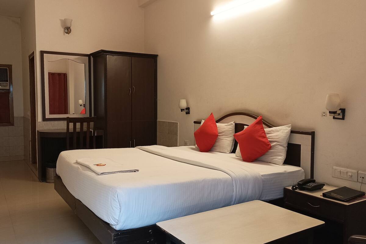 Habitació d'hotel amb un llit, una tauleta de nit, un escriptori, un armari i un bany visible a través d'una porta oberta.