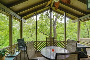 A covered outdoor seating area with a glass table and chairs, surrounded by large windows offering a view of a forested area. - Hot Tub! Golfer's Oasis in Margaritaville Resort (Osage Beach)