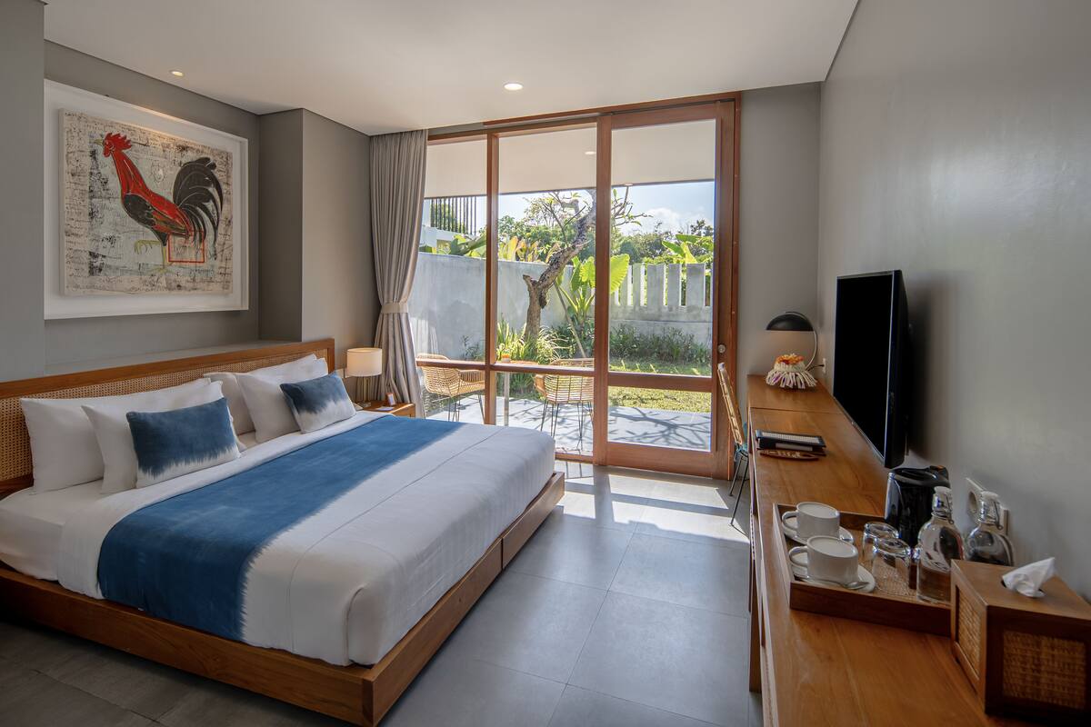 Ein Hotelzimmer mit einem großen Bett, einem Fernseher, einem Esstisch mit Frühstücksangeboten und einem Balkon mit Blick ins Grüne.