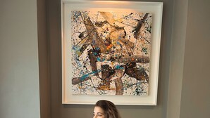 Uma pessoa sentada na cama com uma bandeja de itens de café da manhã, um quadro na parede e uma cabeceira de madeira.