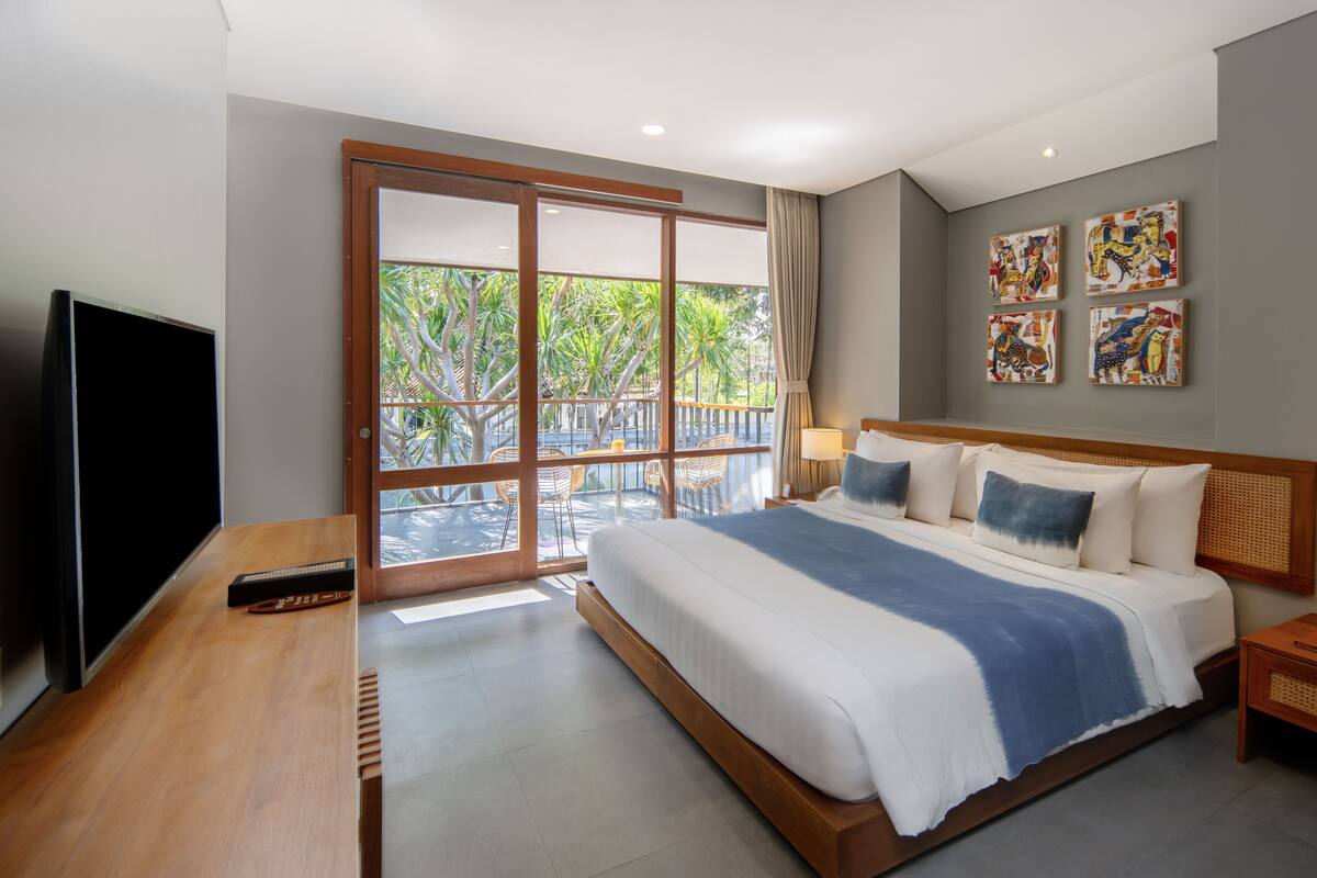 Ein modernes Hotelzimmer mit einem großen Bett, einem Fernseher und einem Balkon mit Blick auf Grünflächen.