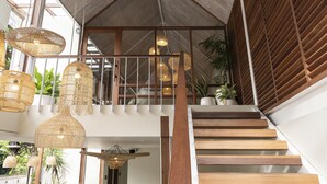 Um interior moderno com escada de madeira, luminárias pendentes de vime e plantas em vasos.