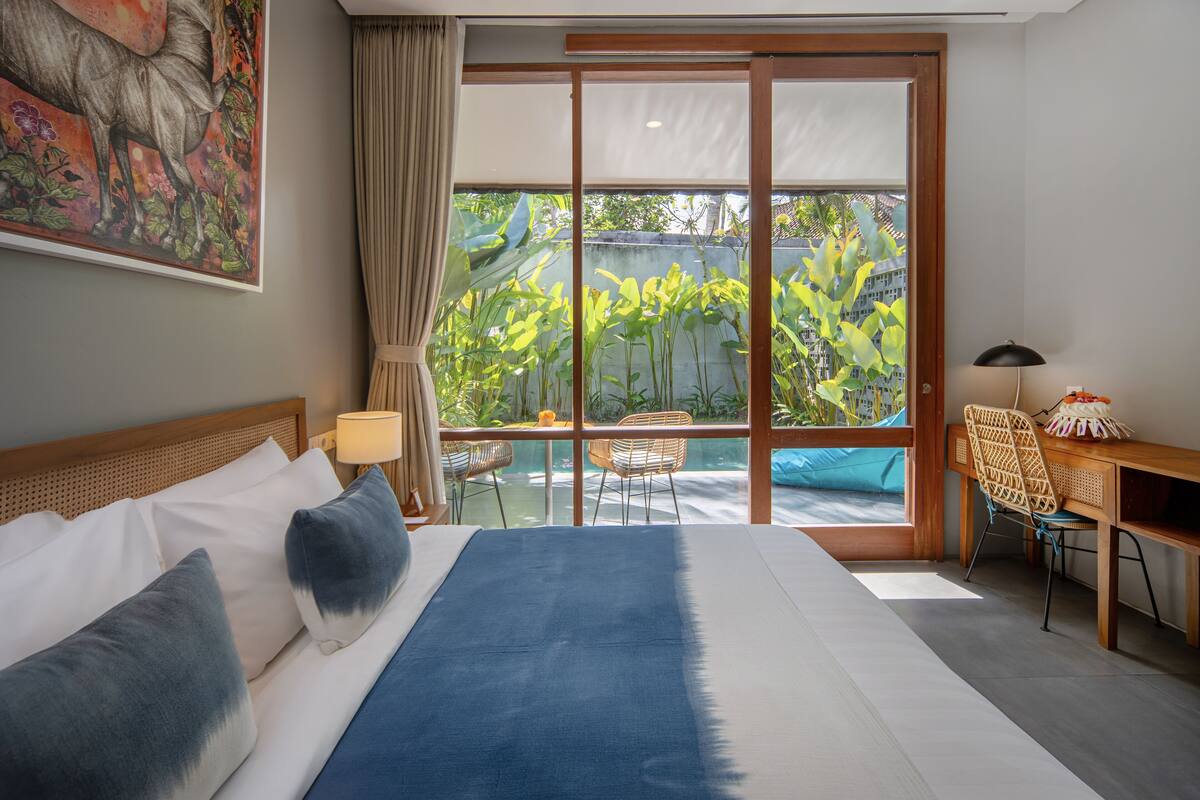 Ein Hotelzimmer mit einem großen Bett, einem Schreibtisch und Blick auf einen Garten durch eine Glastür.