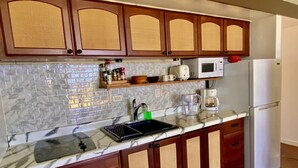 A kitchen with wooden cabinets, a microwave, a coffee maker, and a sink. - Stunning ocean view condo (Maunaloa)