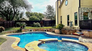 Ein Garten mit Schwimmbad, einer Steinterrasse und einem Haus mit Steinverkleidung.