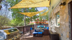 Eine Terrasse mit Grill, Gartenmöbeln und einem Steinhaus im Hintergrund.