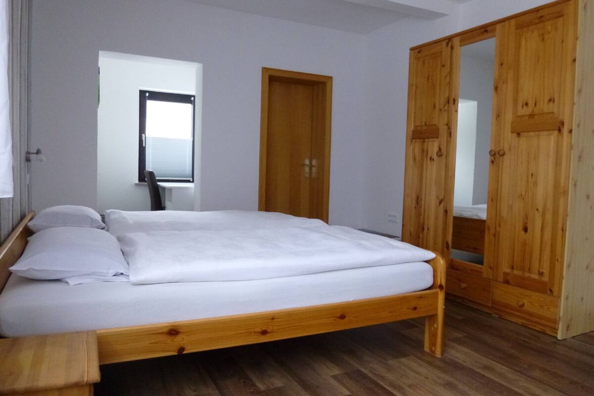 A bedroom with a wooden bed, a wooden wardrobe, and a window with blinds.