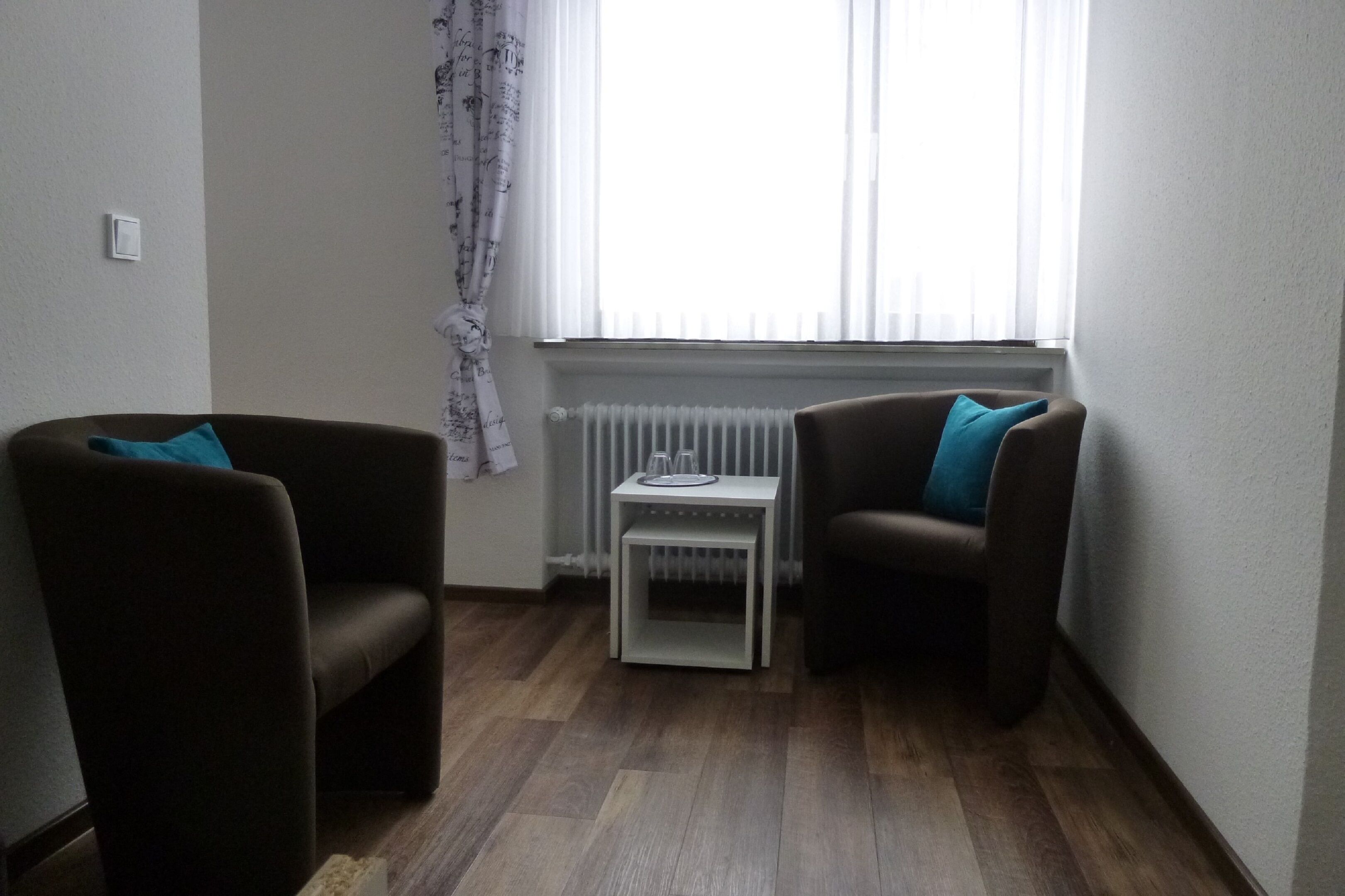 A small, cozy room with two dark brown armchairs, each with a blue pillow, and a white side table between them.