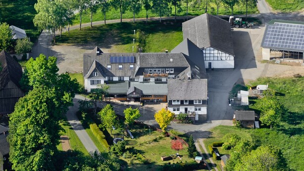 An aerial view of a modern building with a unique architectural design, surrounded by green fields and trees. - Pension Wittgensteiner Schweiz (Bad Berleburg)