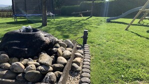 A well-maintained garden with a water feature, a wooden play structure, and a house in the background. - Pension Wittgensteiner Schweiz (Bad Berleburg)