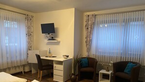 A hotel room with a bed, a desk with a computer, two chairs, a small table, and a window with sheer curtains. - Pension Wittgensteiner Schweiz (Bad Berleburg)