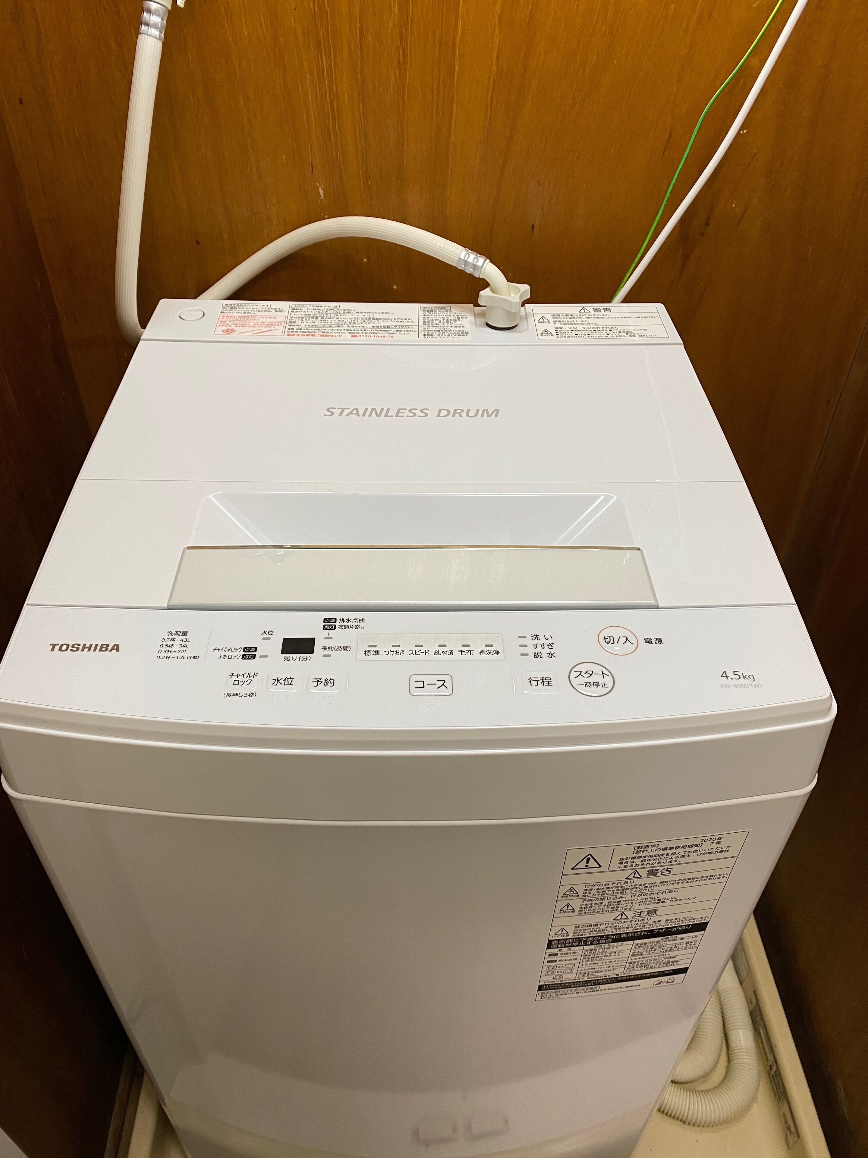 A stainless steel drum washing machine with a control panel, placed in a wooden cabinet.
