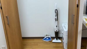 A small, enclosed storage space with a wooden door, a vacuum cleaner, and an iron on the floor. - White Terrace Sakurashinmachi (Tokyo)
