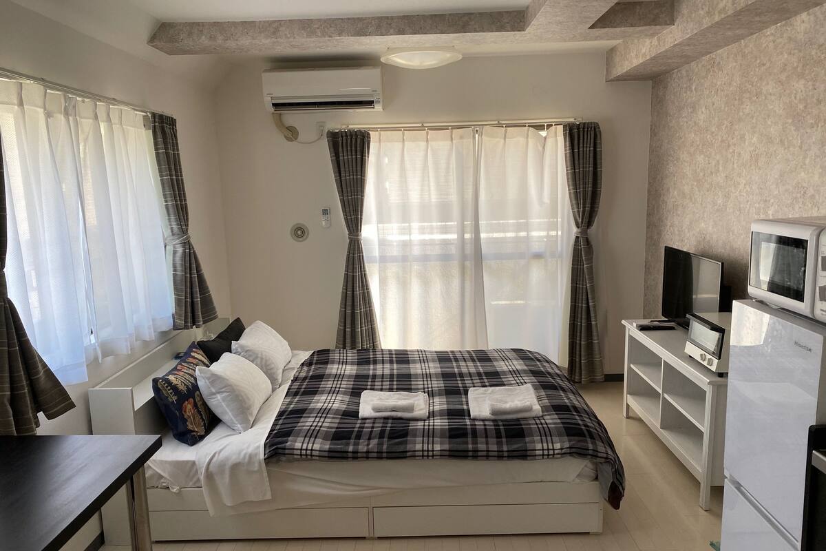 A bedroom with a bed, a desk, a TV, and an air conditioner.