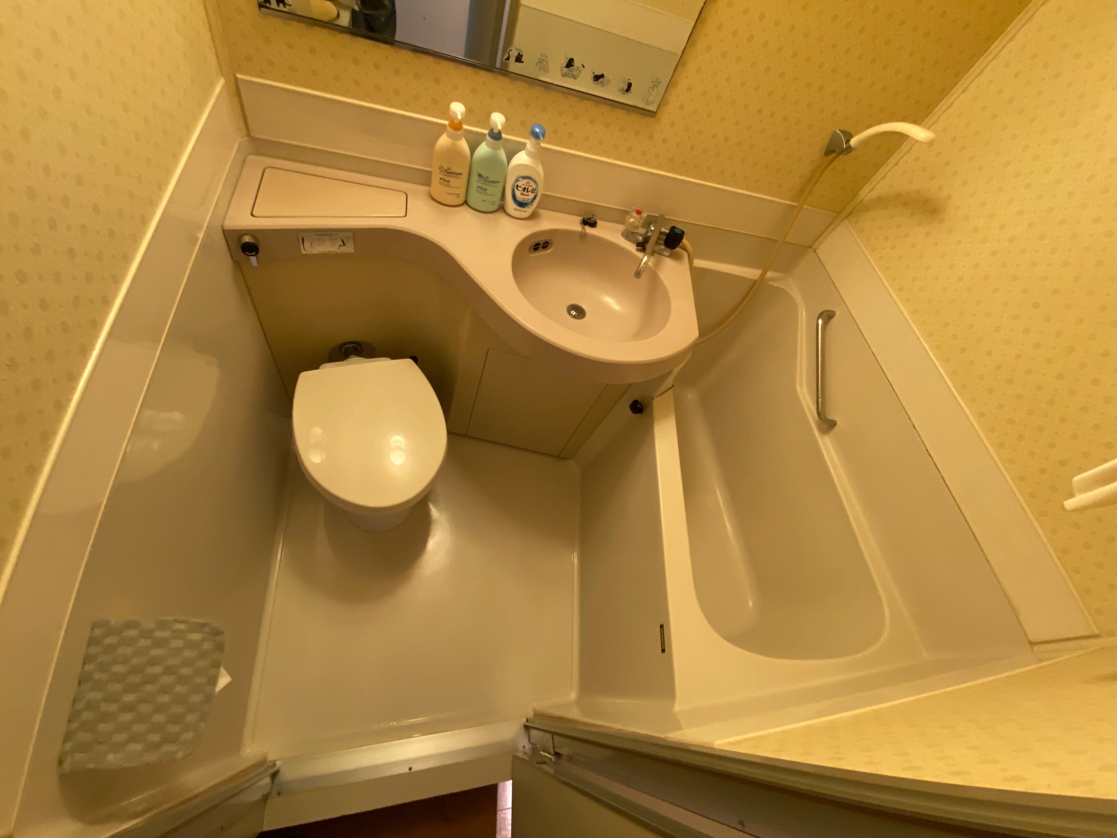 A small bathroom with a toilet, sink, and bathtub. There are three bottles of hand soap on the sink.