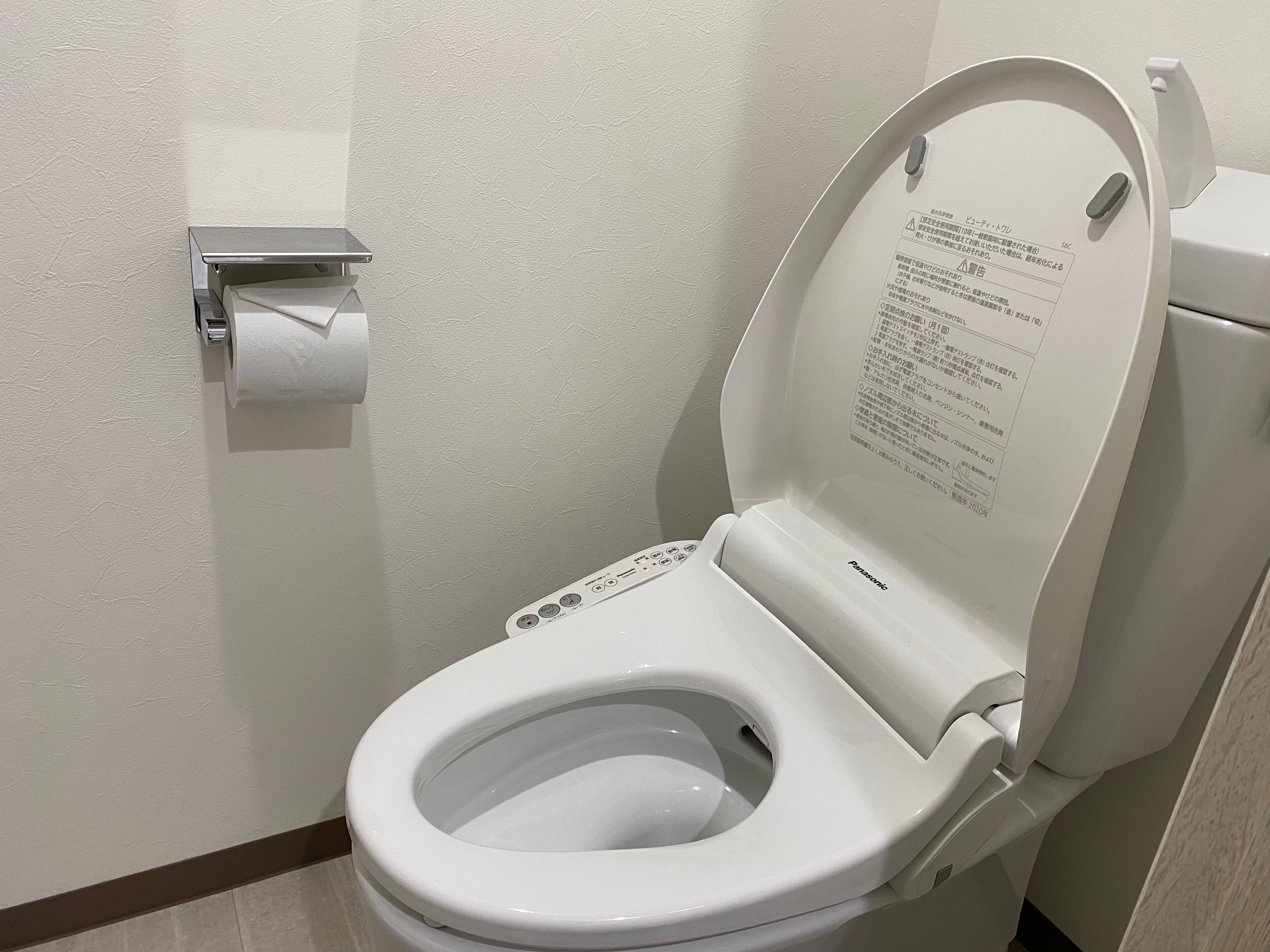 A white toilet with a flush handle and a paper towel dispenser mounted on the wall.