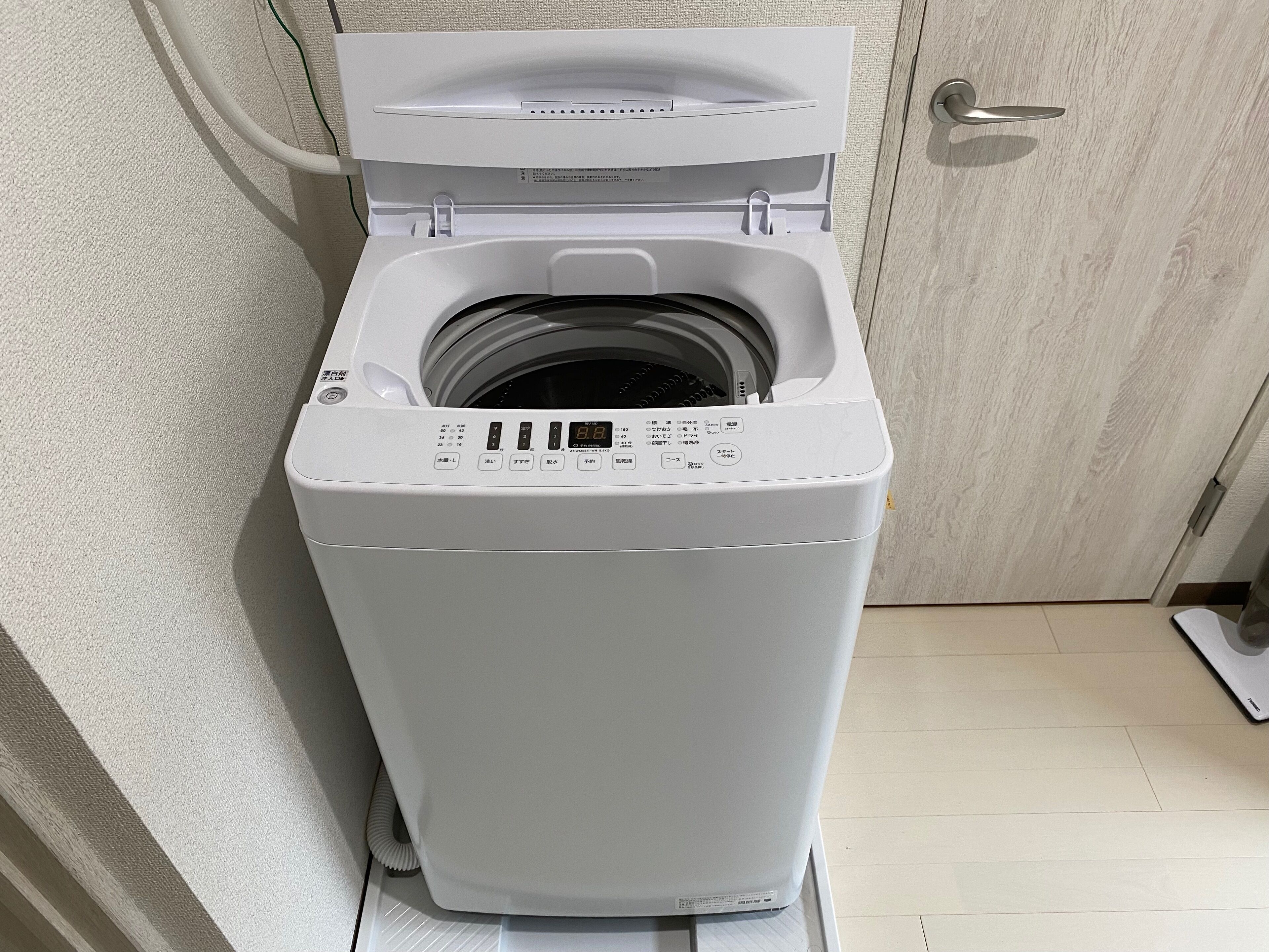 Una lavadora de carga frontal en un baño con puerta de madera y suelo de baldosas.
