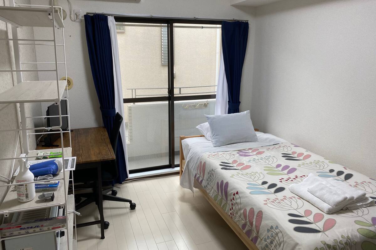 A hotel room with a bed, a desk, and a shelving unit with various items.