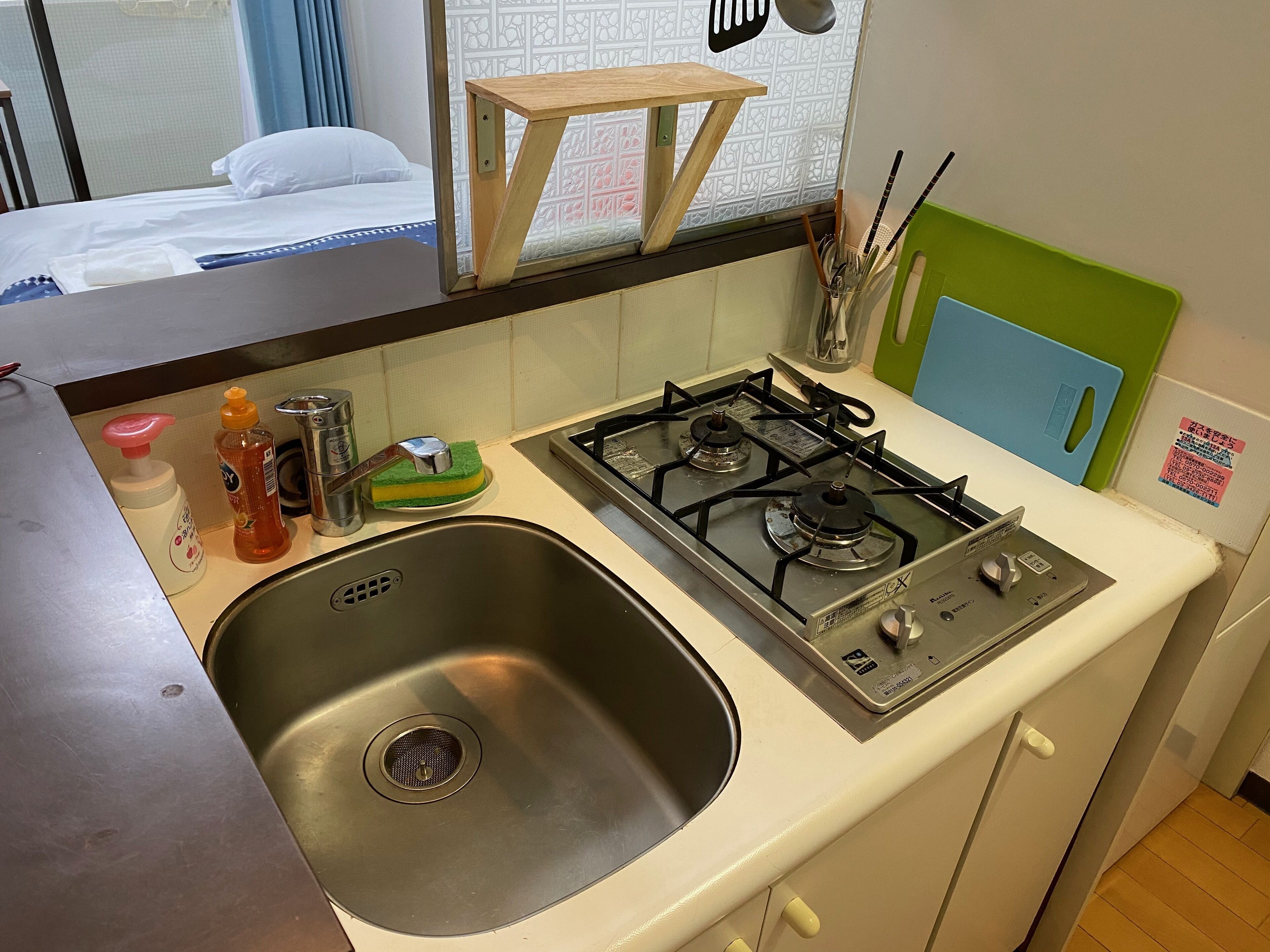 A compact kitchen with a stainless steel sink, a gas stove, and a small wooden stool.