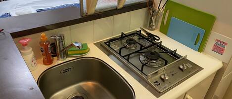 A compact kitchen with a stainless steel sink, a gas stove, and a small wooden stool.
