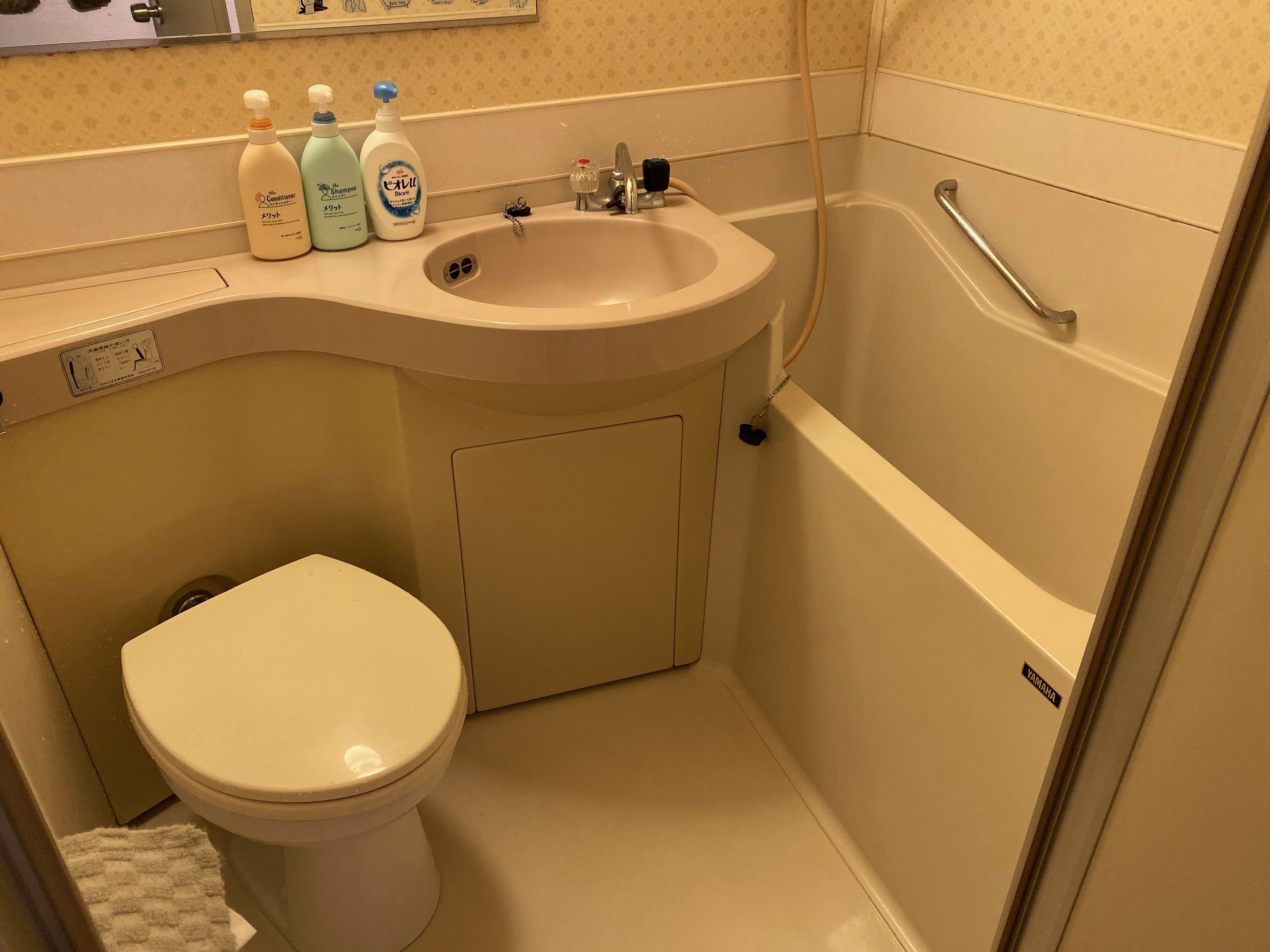 A bathroom with a toilet, sink, and bathtub. There are toiletries on the counter.
