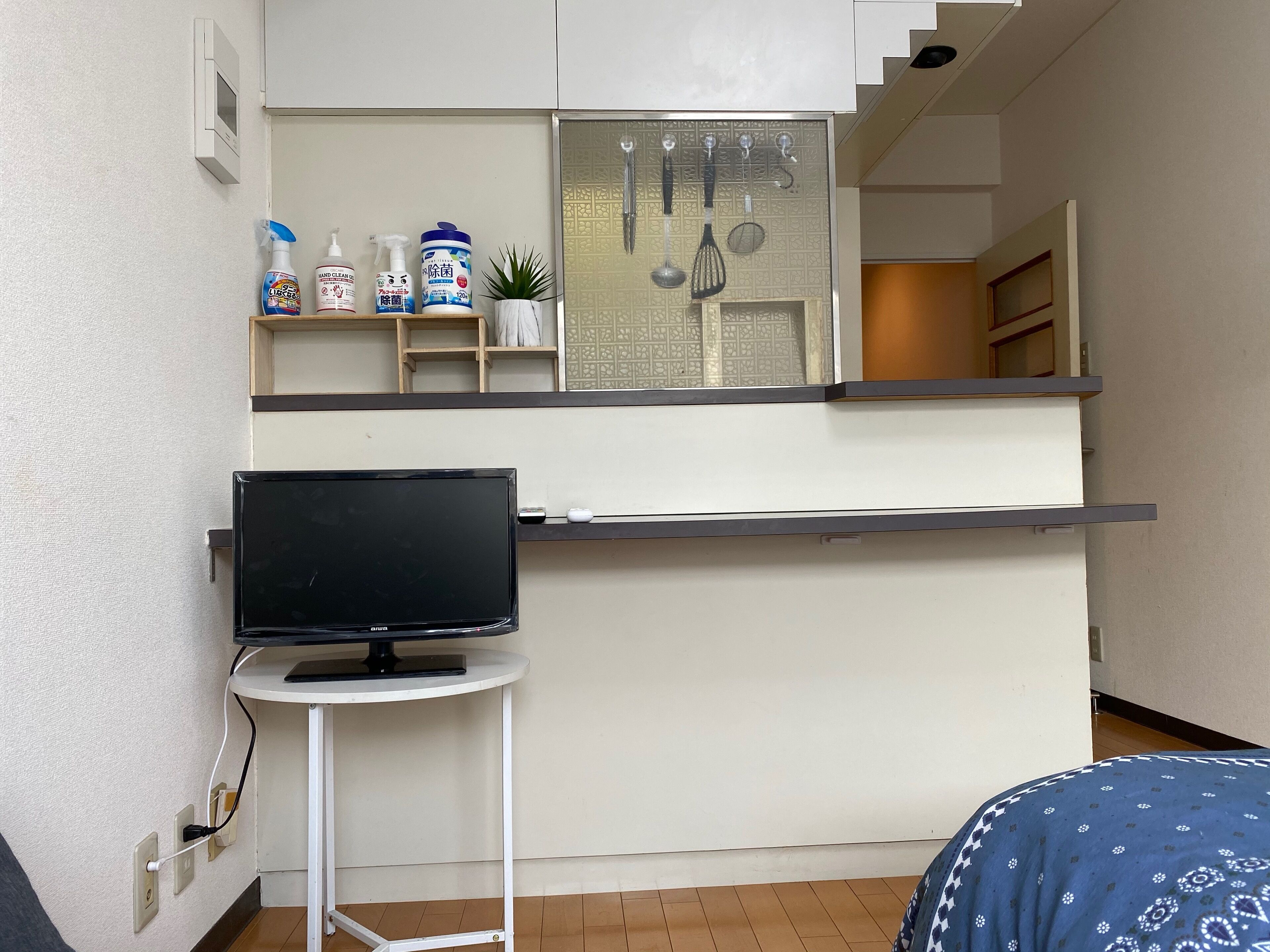 A compact kitchen with a built-in stove, a small table with a television, and a shelf with cleaning supplies.