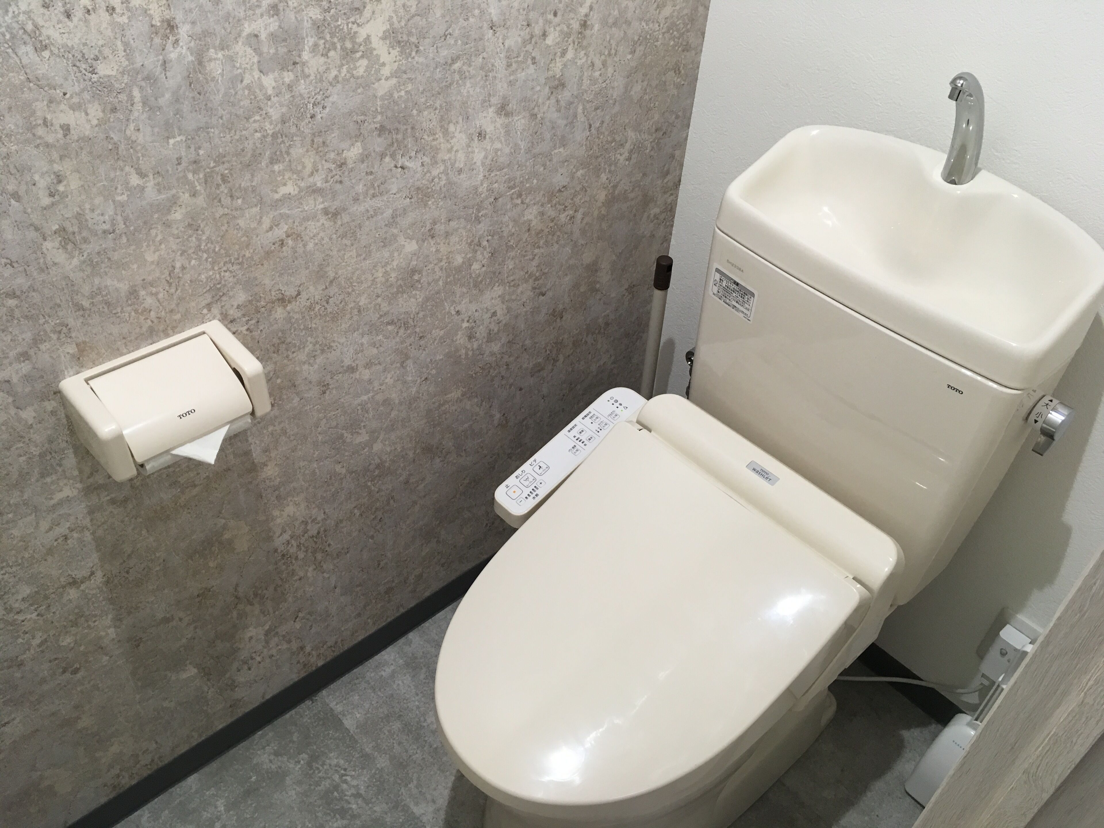 Des toilettes de la marque TOTO, un porte-rouleau de papier toilette fixé au mur et un lavabo de la marque TOTO.