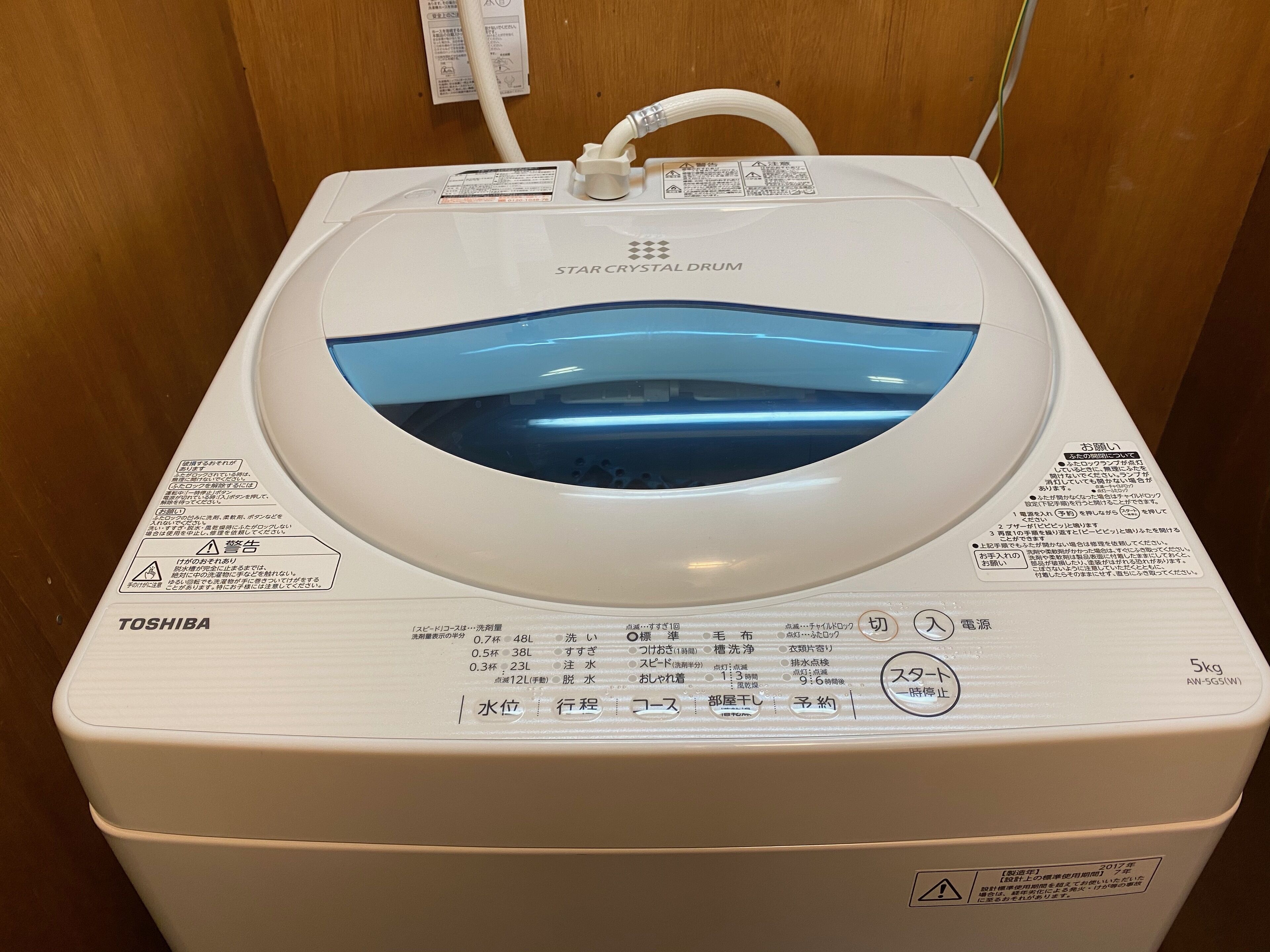 Lavadora Toshiba Star Crystal Drum blanca con tanque de agua transparente, panel de control e instrucciones de seguridad.