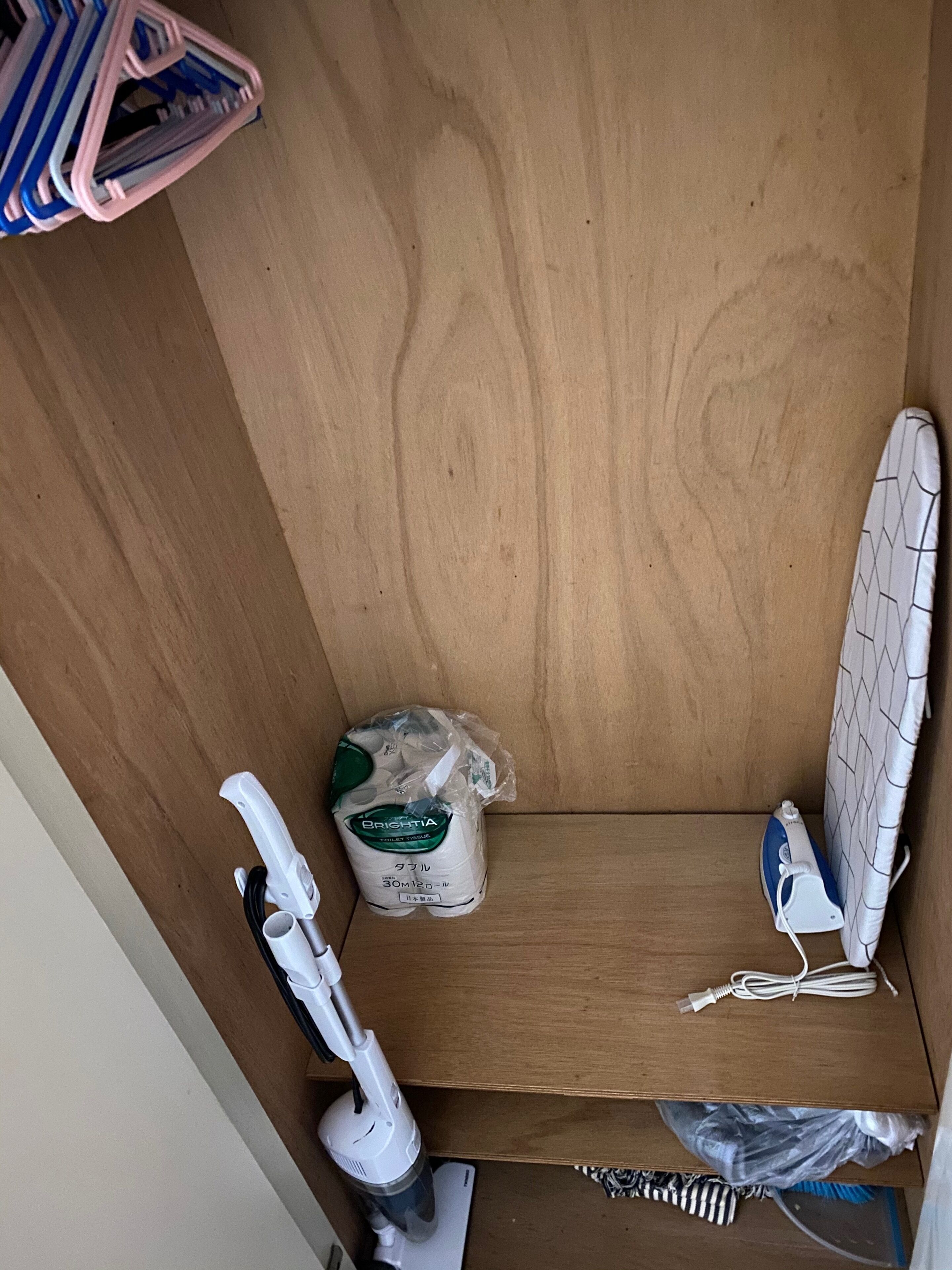 A wooden cabinet with a white iron, a vacuum cleaner, and a package of toilet paper.