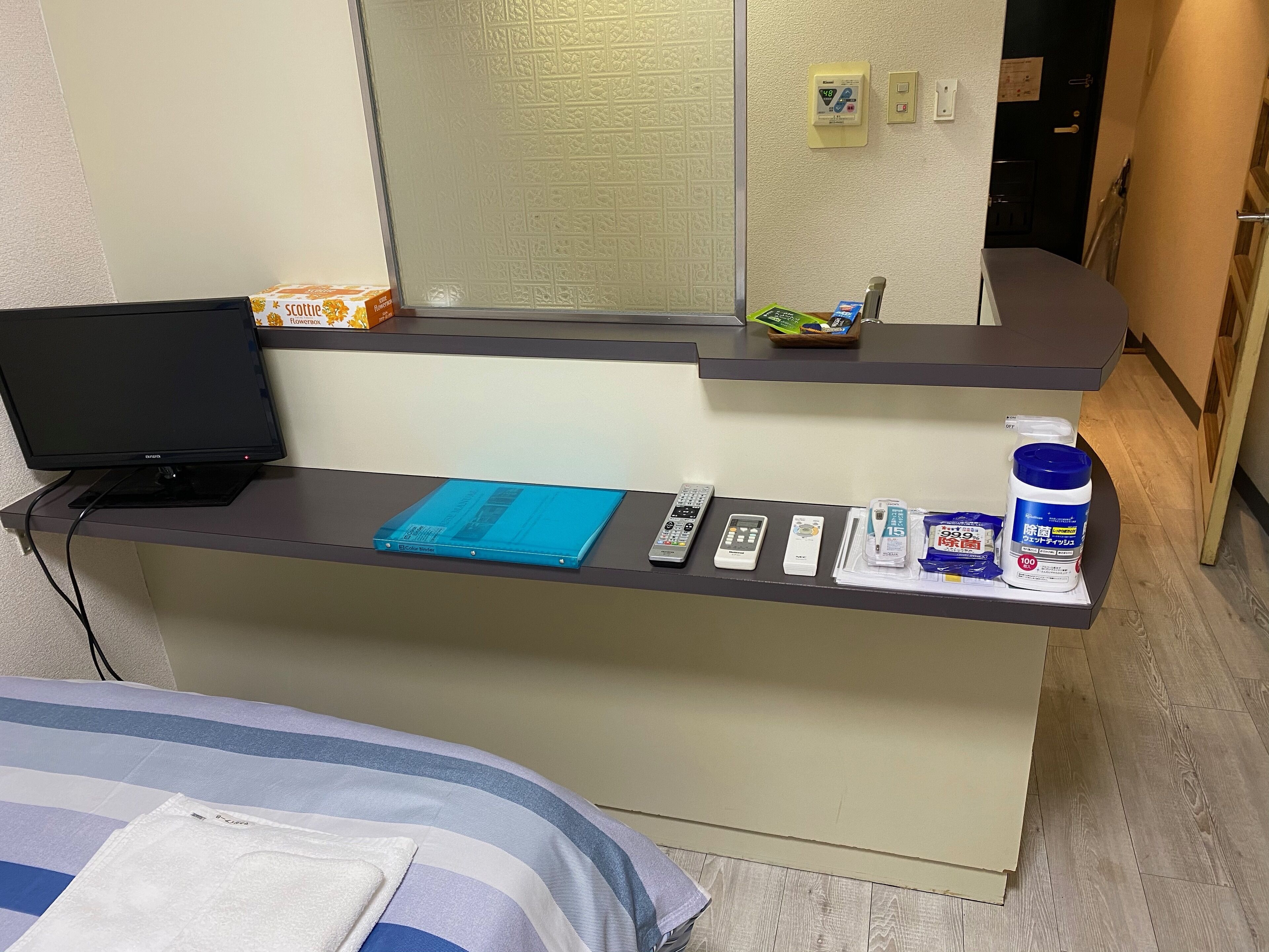A hotel reception desk with a laptop, remote controls, a blue booklet, and toiletries.