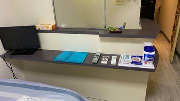 A hotel reception desk with a laptop, remote controls, a blue booklet, and toiletries.