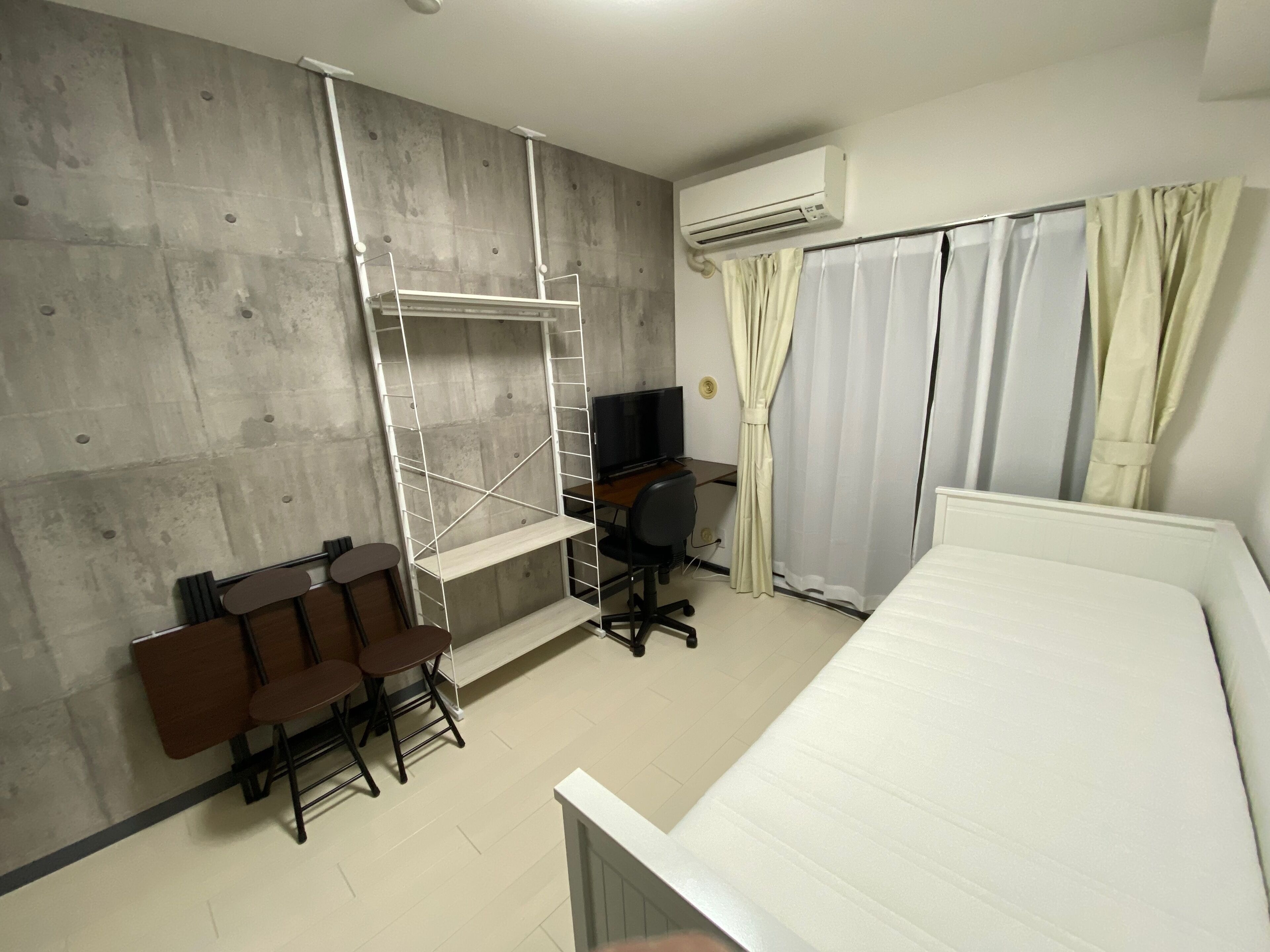 A room with a bed, a desk with a chair, a TV, and a window with curtains.