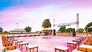 An outdoor seating area with tables and benches, a stage with lighting, and a desert-themed backdrop. - Treebo Desert Harmony Camp (Jaisalmer)