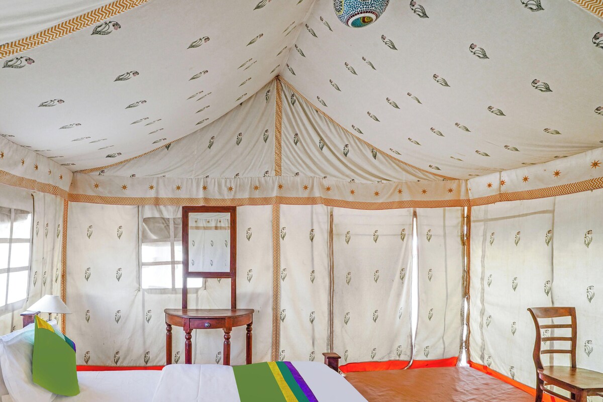 A tent-style room with a bed, chairs, a table, and a mirror.