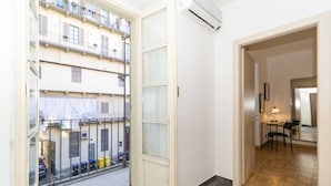 A room with a large window, a door leading to a balcony, a small table with chairs, and an air conditioning unit. - GuestHost - Comfortable apartment that can accommodate up to 4 people with great ease and is equipped with every kind of comfort. We are in the beating heart of Turin, Piazza Vittorio Veneto, overlooking the Turin hill and the Gran Madre, everything is c (Turin)