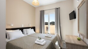 Quarto de hotel com duas camas, uma escrivaninha, televisão e varanda com cortinas.