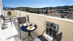 Uma varanda com duas cadeiras, uma mesa e vista para uma cidade.
