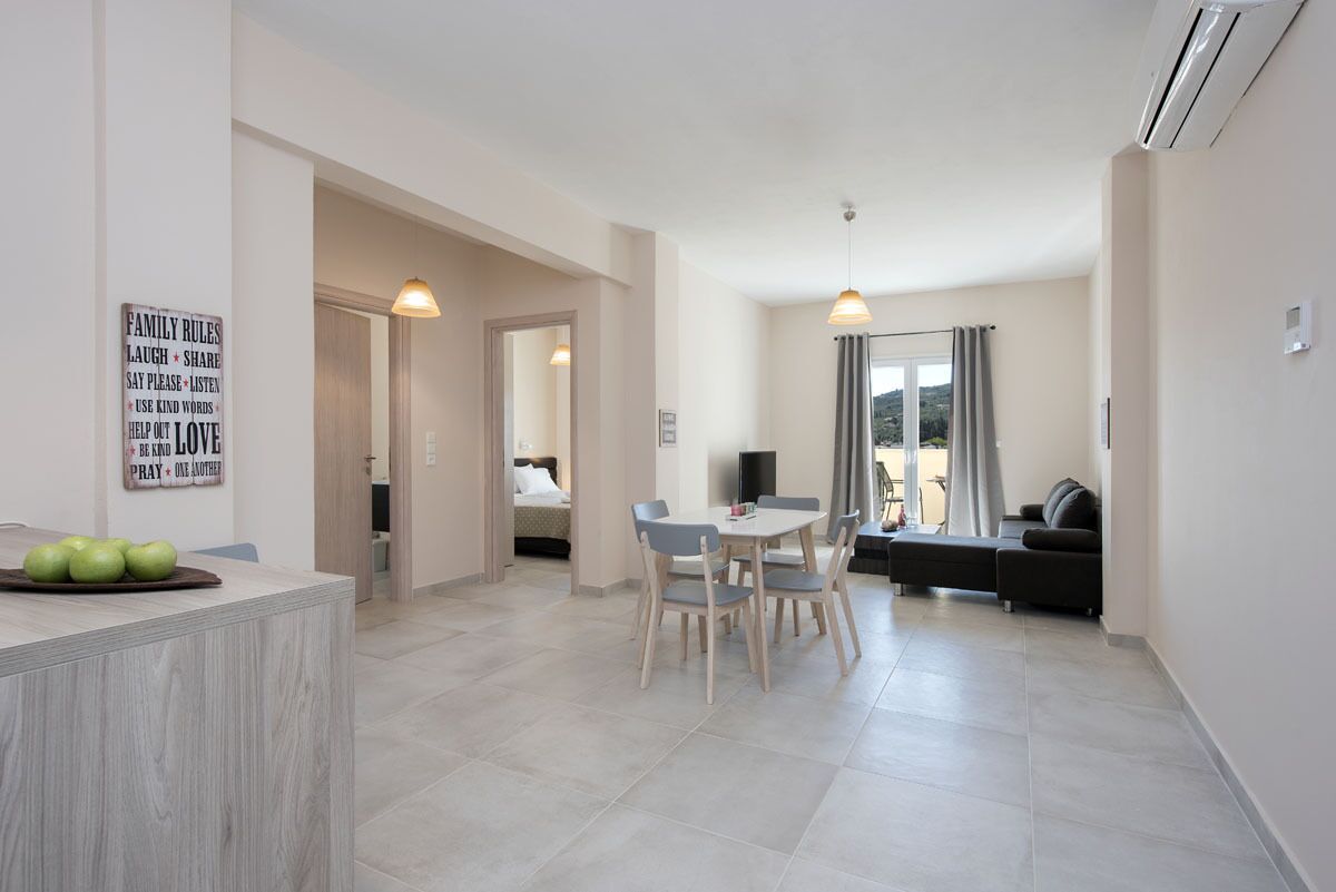 A modern living room with a dining area, a sofa, and a TV. There is a sign on the wall with family rules.
