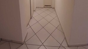 Um corredor estreito com paredes brancas e chão de azulejos.
