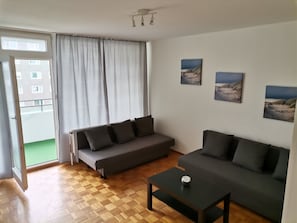 A modern living room with a grey sofa, a smaller grey sofa, and a coffee table. There are three framed pictures on the wall. - 2 bedroom apartment in hanover (Hannover)